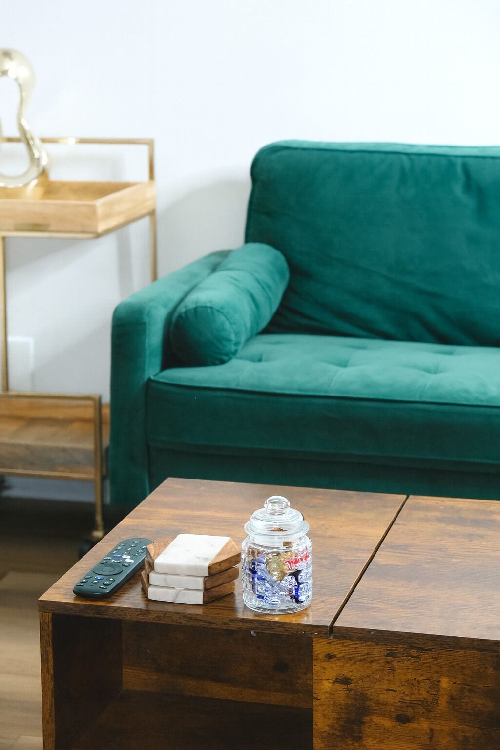 Una mesa de centro de madera con un control remoto, un tarro de caramelos y una caja blanca.