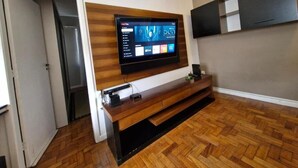 A modern living room with a mounted flat-screen TV, wooden entertainment center, and a herringbone-patterned wooden floor. - SUH Copacabana 89 Beach View (Rio de Janeiro)