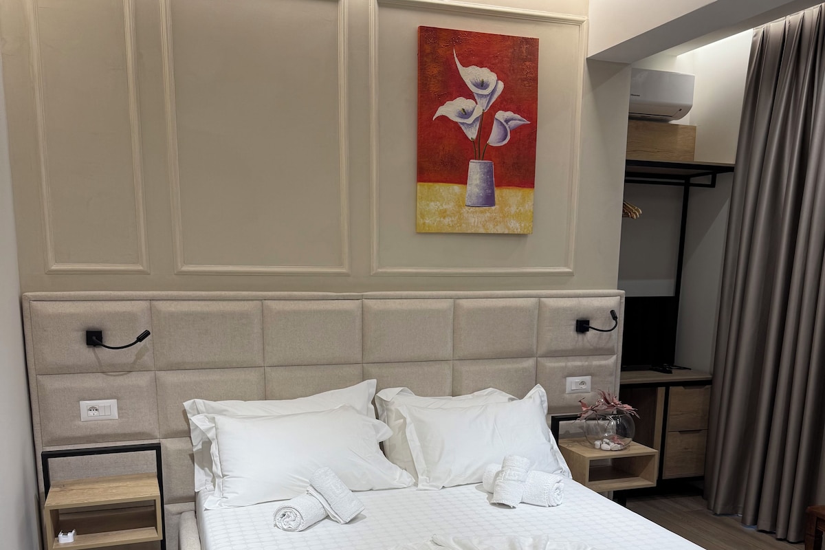 Een hotelkamer met een groot bed, een nachtkastje, een schilderij aan de muur en een airconditioningunit aan het plafond.