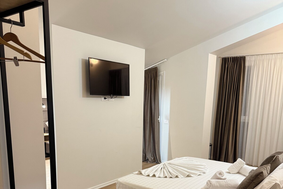 Een moderne hotelkamer met een bed, een aan de muur bevestigde televisie, een houten vloer en een kledingkast met spiegel.