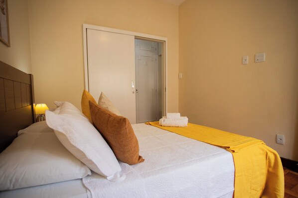 A hotel room with a bed, pillows, a yellow blanket, and a door. - SUH Copacabana 76 (Rio de Janeiro)