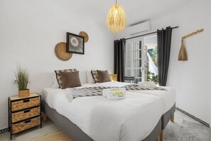 A modern bedroom with a bed, bedside tables, a hanging light fixture, and a view through a window.