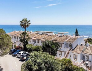 A coastal residential area with white buildings, a clear blue sky, and the sea in the background.