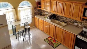 Una cocina con armarios de madera, una encimera, un fregadero y una estufa. Hay una ventana con cortinas y una mesa con dos sillas.