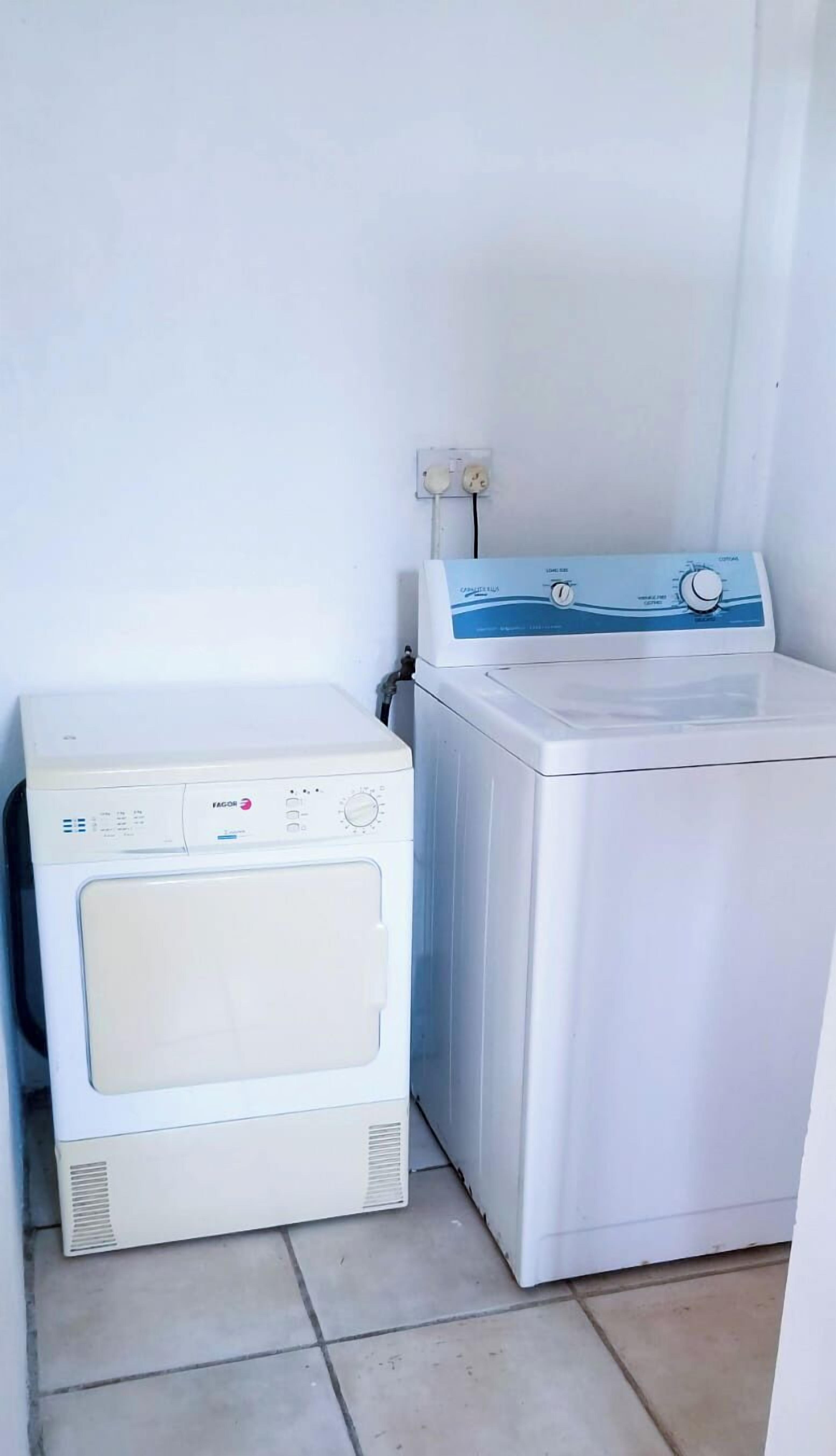 A laundry area with a front-loading washer and dryer, a power outlet, and a tiled floor.