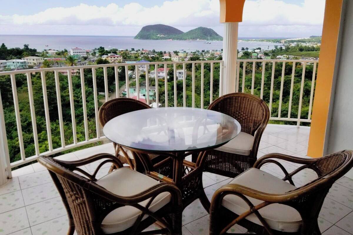 Un balcon avec une table ronde et des chaises en osier, donnant sur une ville côtière et la mer.