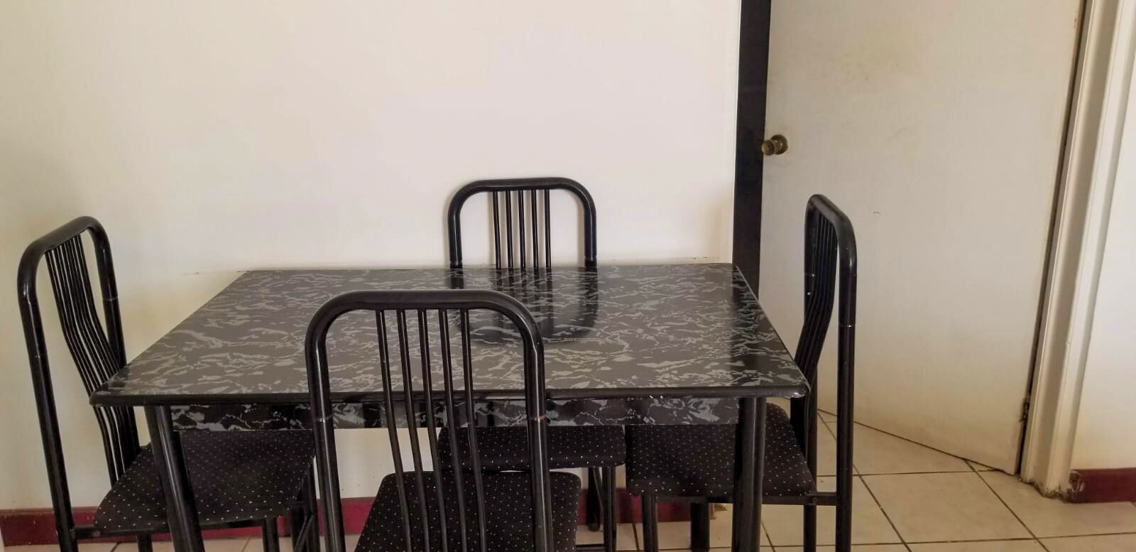 Una mesa de comedor con cuatro sillas, una puerta y un piso de baldosas.