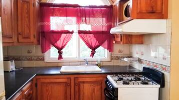 Cocina compacta con gabinetes de madera, estufa a gas, lavamanos y una ventana con cortinas rojas.