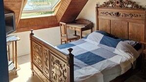 A bedroom with a sloped ceiling, a wooden bed with intricate headboard, a desk, and a chair.
