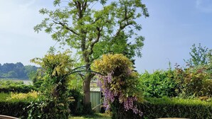 A garden entrance with a wooden gate, a pathway leading to a building, and a view of a tree and landscape.