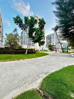 A residential area with high-rise buildings, a paved walkway, and green lawns. - Coral Escape | Beachfront + pool + ocean view (Isla Verde)