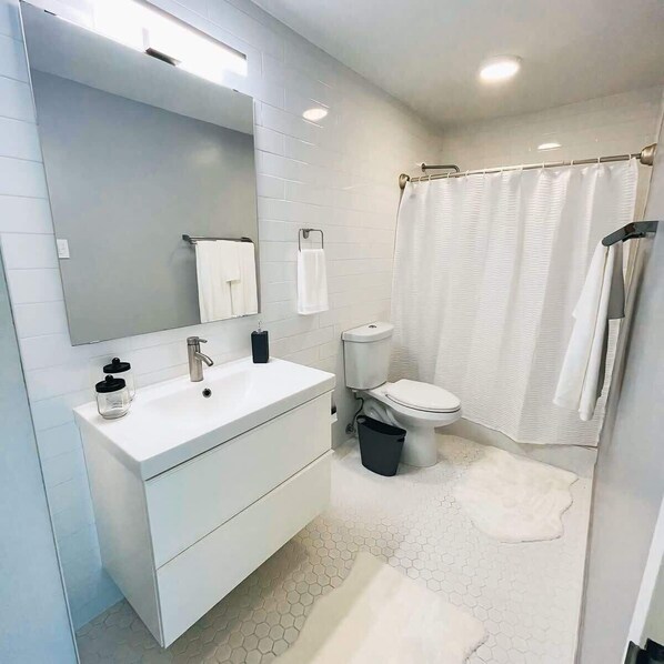 A modern bathroom with a white sink, mirror, and toilet, and a shower curtain.