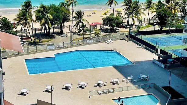 A rooftop pool with multiple sections, a beach view, and palm trees.