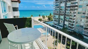 A balcony with a white table and chairs, overlooking a beach and ocean.
