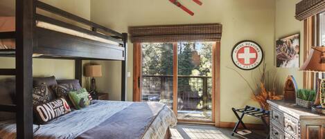 A cozy bedroom with a bunk bed, a desk, and a window overlooking a deck.