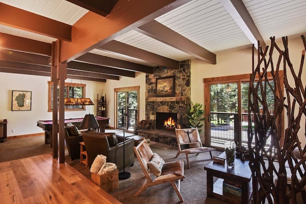 A cozy living room with a stone fireplace, wooden beams, and a pool table.
