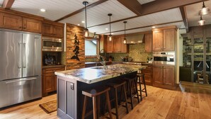 A spacious kitchen with wooden cabinets, a large island with bar stools, stainless steel appliances, and a stone backsplash. - Kingswood Luxury Home with Hot Tub, Backs to Forest (Kings Beach)