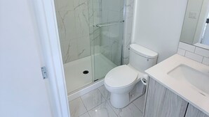 Une salle de bain moderne avec une douche à parois de verre, des toilettes blanches et un meuble-lavabo.