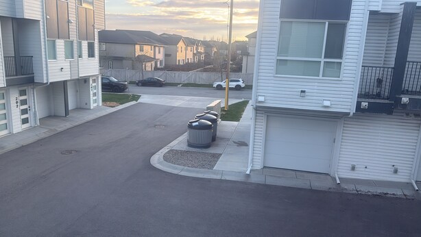 Une rue résidentielle bordée de maisons, avec un trottoir et des poubelles.