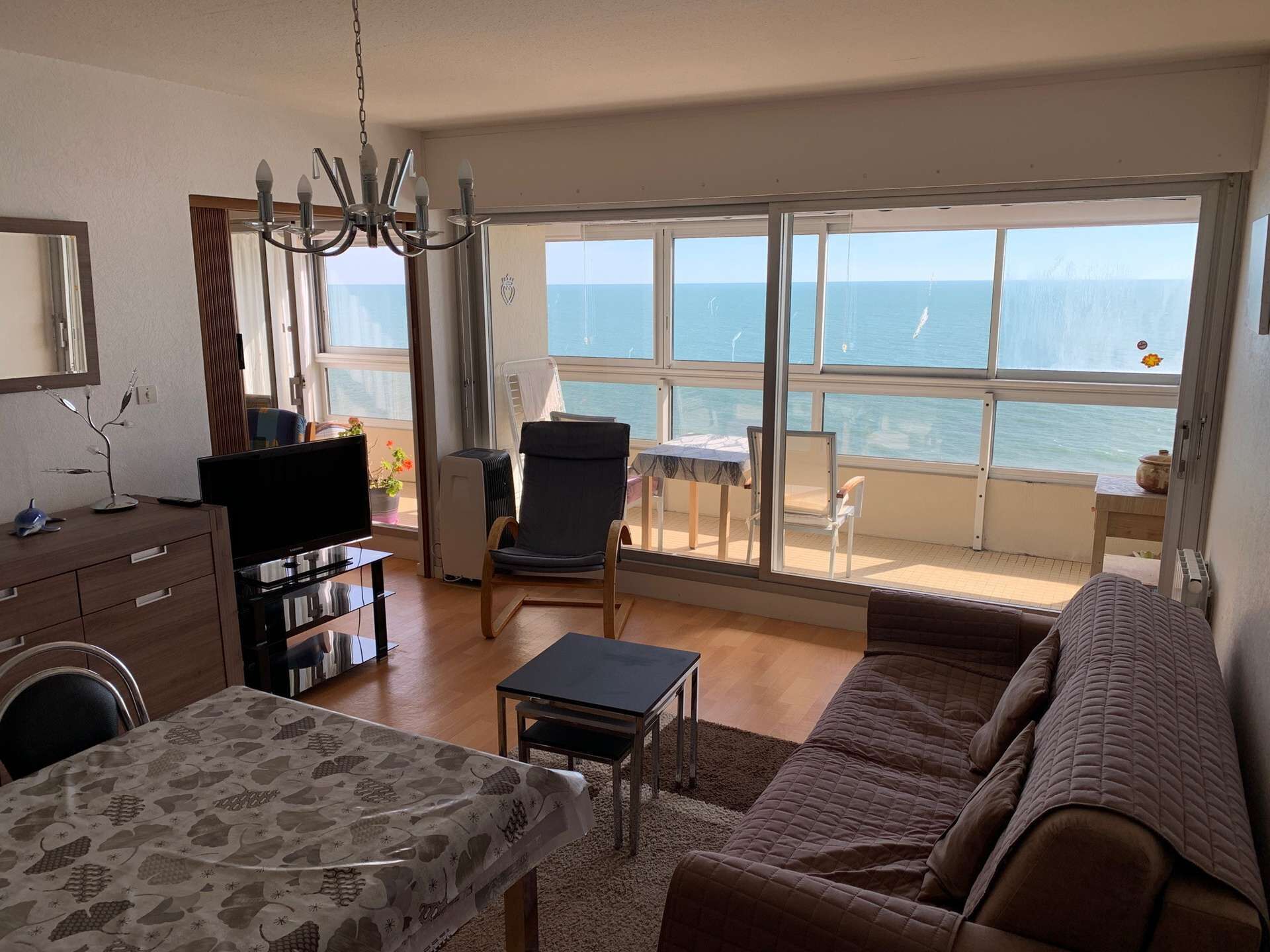 Un salon comprenant un canapé, une table à manger, un téléviseur et une grande fenêtre donnant sur la mer.