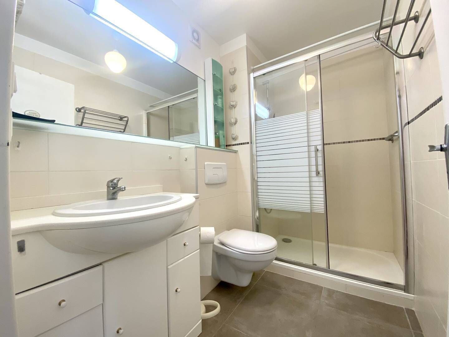 A modern bathroom with a white sink, toilet, and glass-enclosed shower.