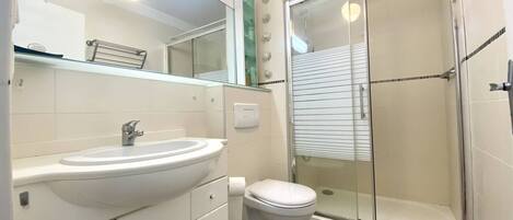 A modern bathroom with a white sink, toilet, and glass-enclosed shower.