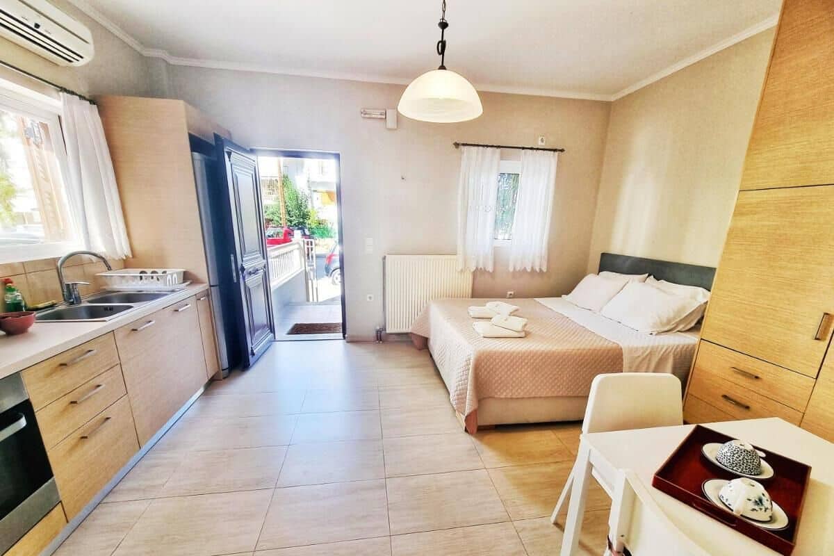 A compact hotel room with a kitchenette, a bed, a small table with a tray, and a view of the outside.