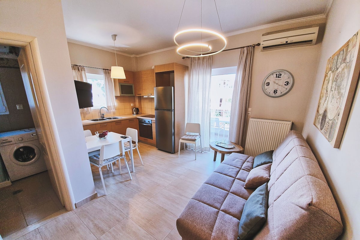 A modern kitchen with a dining area, a living room with a sofa, and a laundry machine.