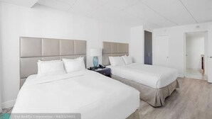 Una habitación de hotel con dos camas, una mesita de noche y una puerta que da a otra habitación.