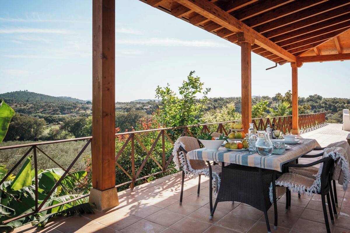 A covered outdoor dining area with a table set for two, overlooking a scenic landscape.