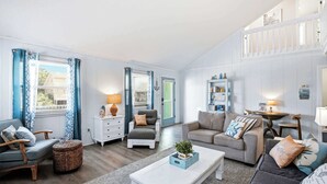 A spacious living room with a sofa, armchair, and coffee table, a small side table, and a bookshelf. - The Salty Rooster by Brunswick Vacation Rentals: New Pool & Renovated Bedrooms (Ocean Isle Beach)
