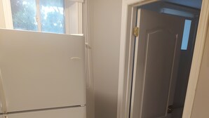 Une cuisine avec un réfrigérateur blanc, une porte donnant sur une autre pièce et un sol carrelé.