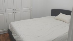 Une chambre à coucher avec un lit, un plancher en bois, des murs blancs et une armoire.