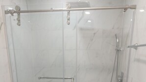 Une douche fermée par des parois de verre, dotée d’une barre d’appui, des toilettes et un sol recouvert de carreaux de marbre.
