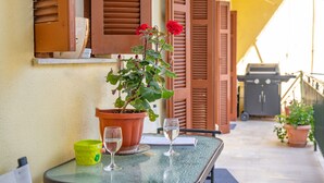 A table with a potted plant, two glasses of water, and a notebook on a balcony with wooden shutters and a yellow wall. - Anthia: Balcony and BBQ, 3 min to Airport, WiFi, Aircon (Kanoni)