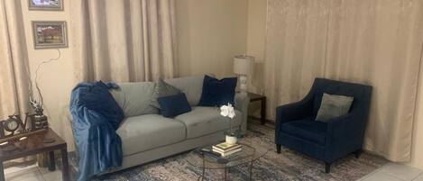 A living room with a sofa, armchair, coffee table, and curtains.