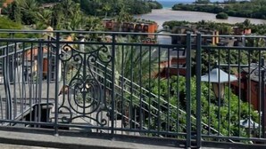 Un balcón con barandilla de hierro forjado con vistas a un paisaje costero con edificios y vegetación.