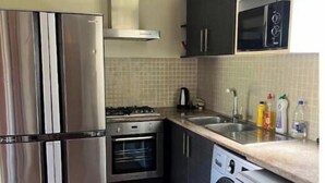 Una cocina compacta con refrigerador, horno, microondas y lavadora de acero inoxidable.