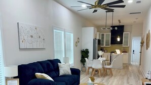 Una sala moderna con un sofá azul oscuro, una mesa de centro redonda de madera y un comedor con sillas blancas.