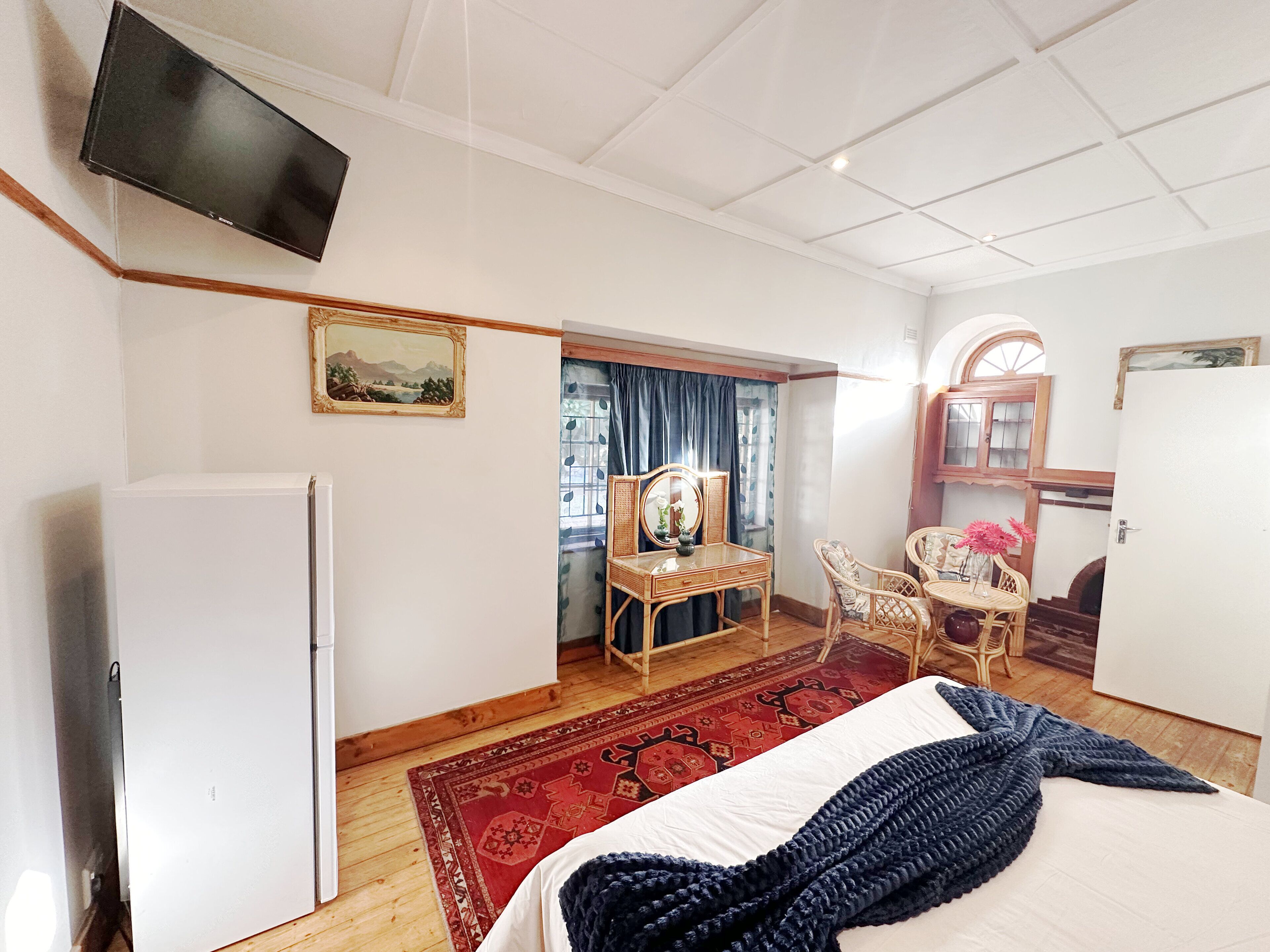 Ett rum med en säng, en tv, ett skrivbord med en stol och ett fönster med gardiner.