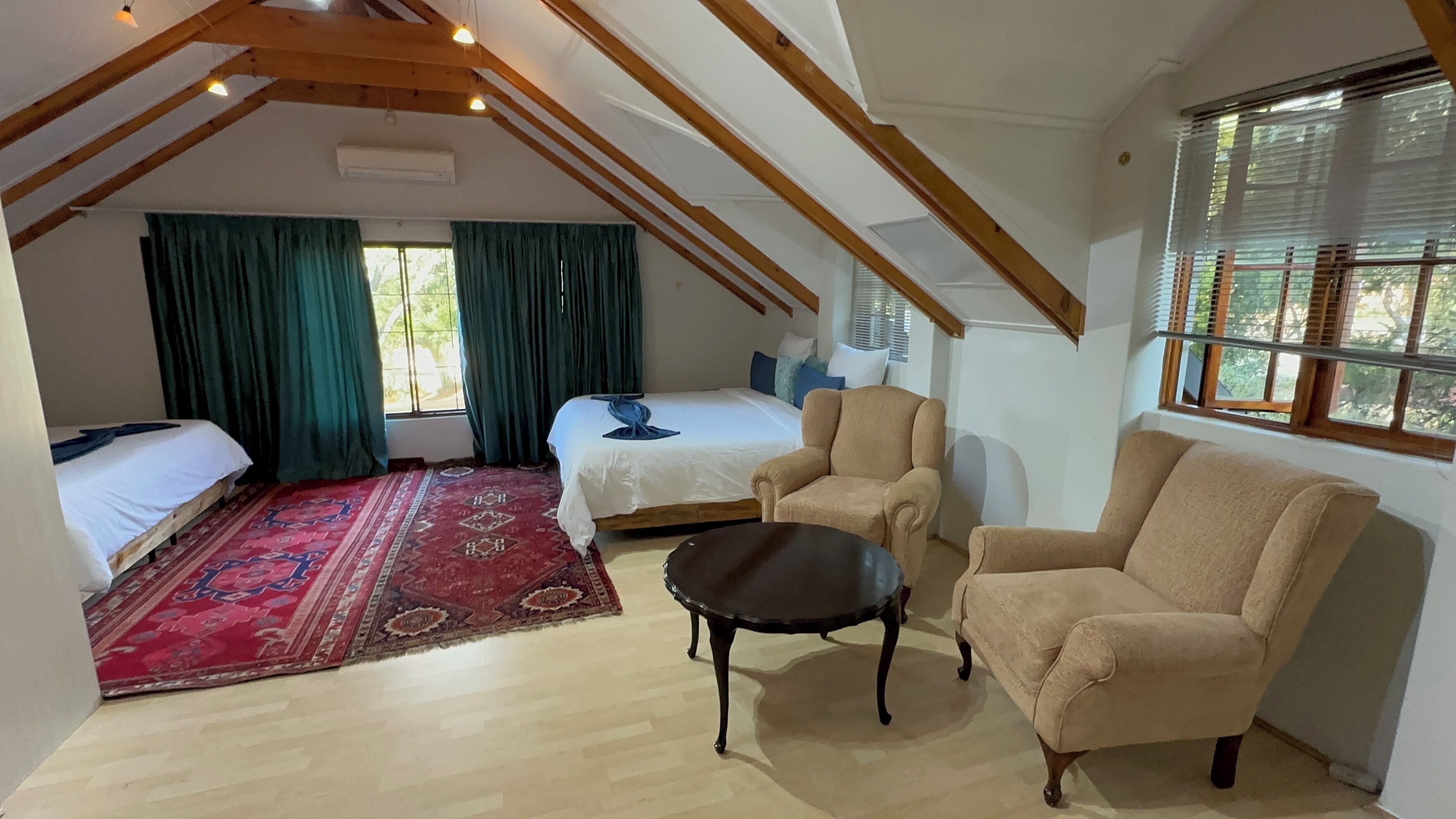Una habitación con techo alto, vigas de madera, una cama, un sofá, una mesita y una ventana con persianas.
