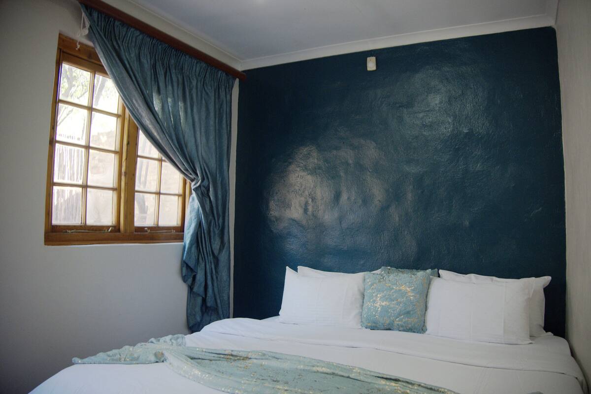 Une chambre avec un grand lit, une fenêtre avec des rideaux et un mur bleu foncé.
