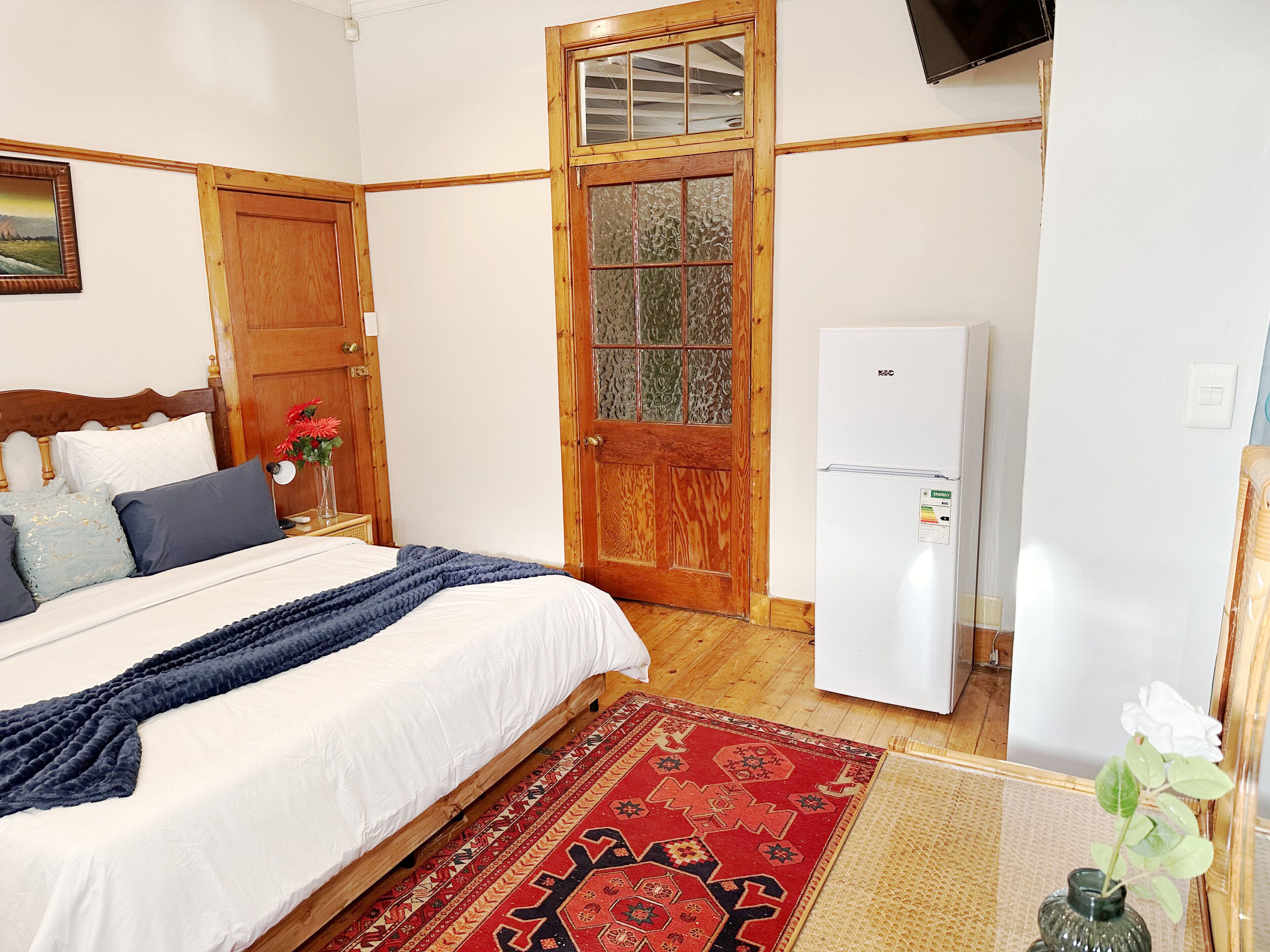 A bedroom with a bed, a wooden door, a white refrigerator, and a painting on the wall.