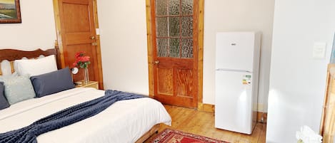 A bedroom with a bed, a wooden door, a white refrigerator, and a painting on the wall.