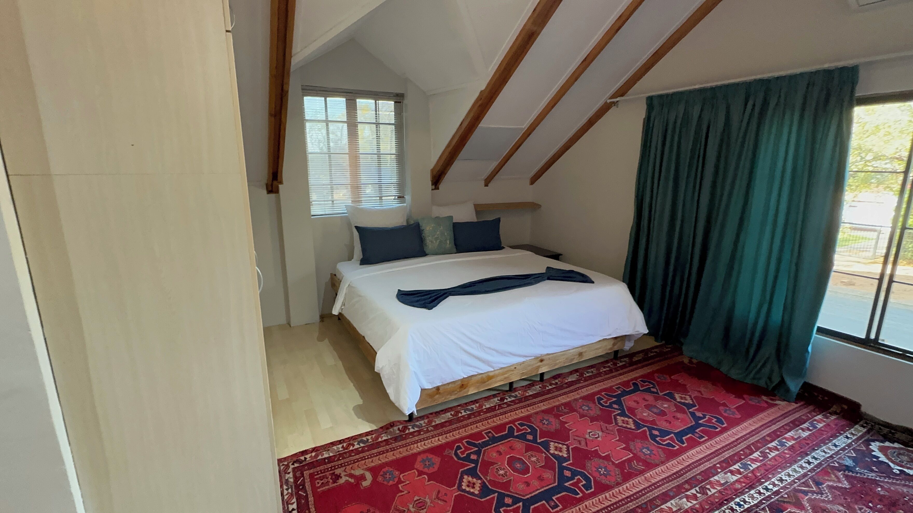 A bedroom with a bed, a window with blinds, a green curtain, and a patterned rug.