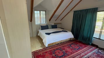 A bedroom with a bed, a window with blinds, a green curtain, and a patterned rug.