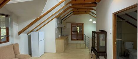 A spacious loft with a high ceiling, wooden beams, a kitchenette, a dining area, and a living room with a sofa.