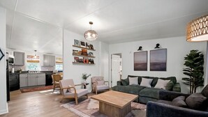 A modern living room with a wooden coffee table, a green sofa, and a dining area with a kitchen in the background.