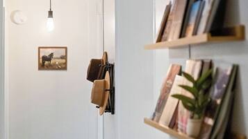 Un pasillo con una puerta, una lámpara, un cuadro enmarcado y una estantería con libros y una planta.