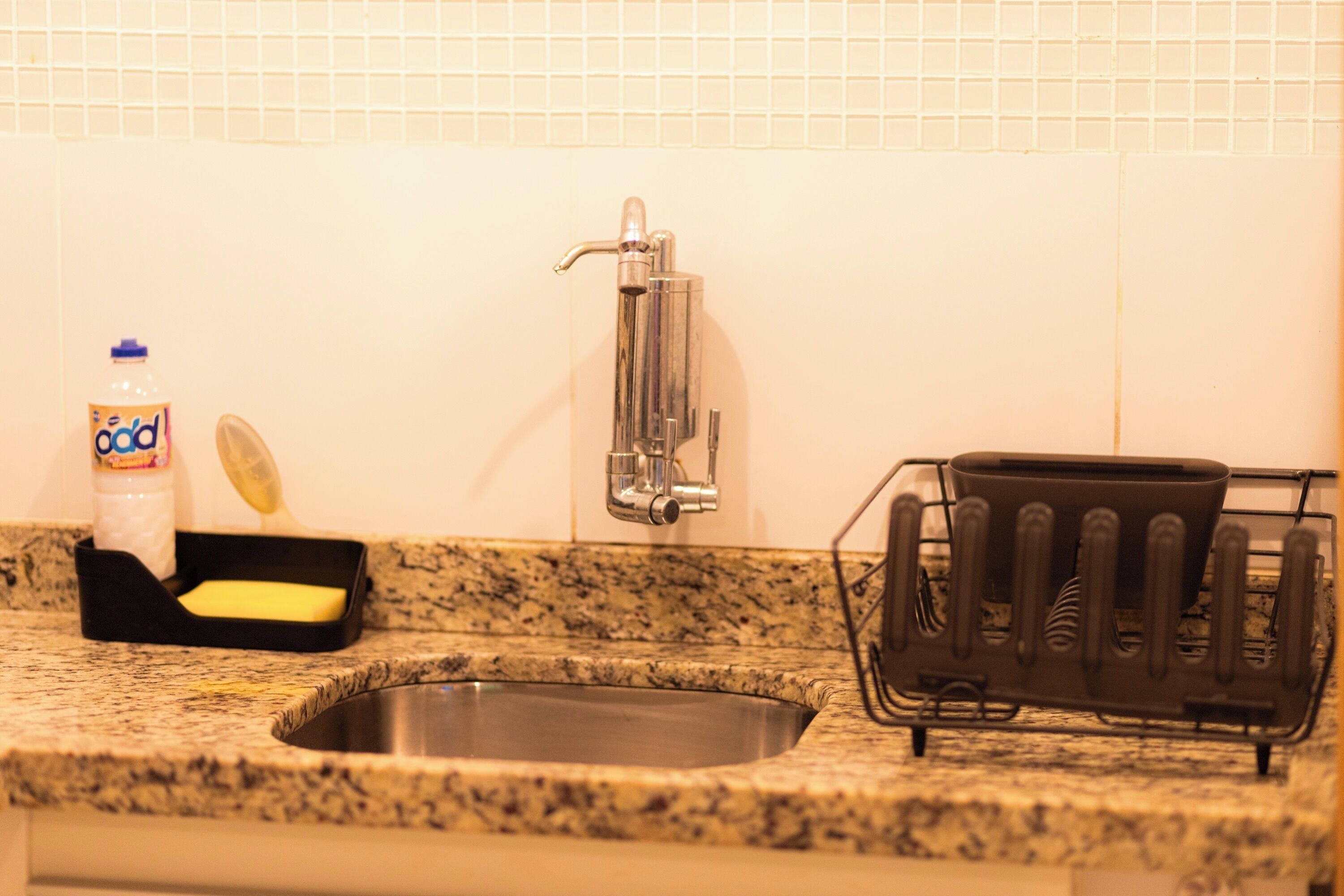 A kitchen with a granite countertop, a stainless steel sink, a soap dispenser, a dish soap bottle, and a dish rack.